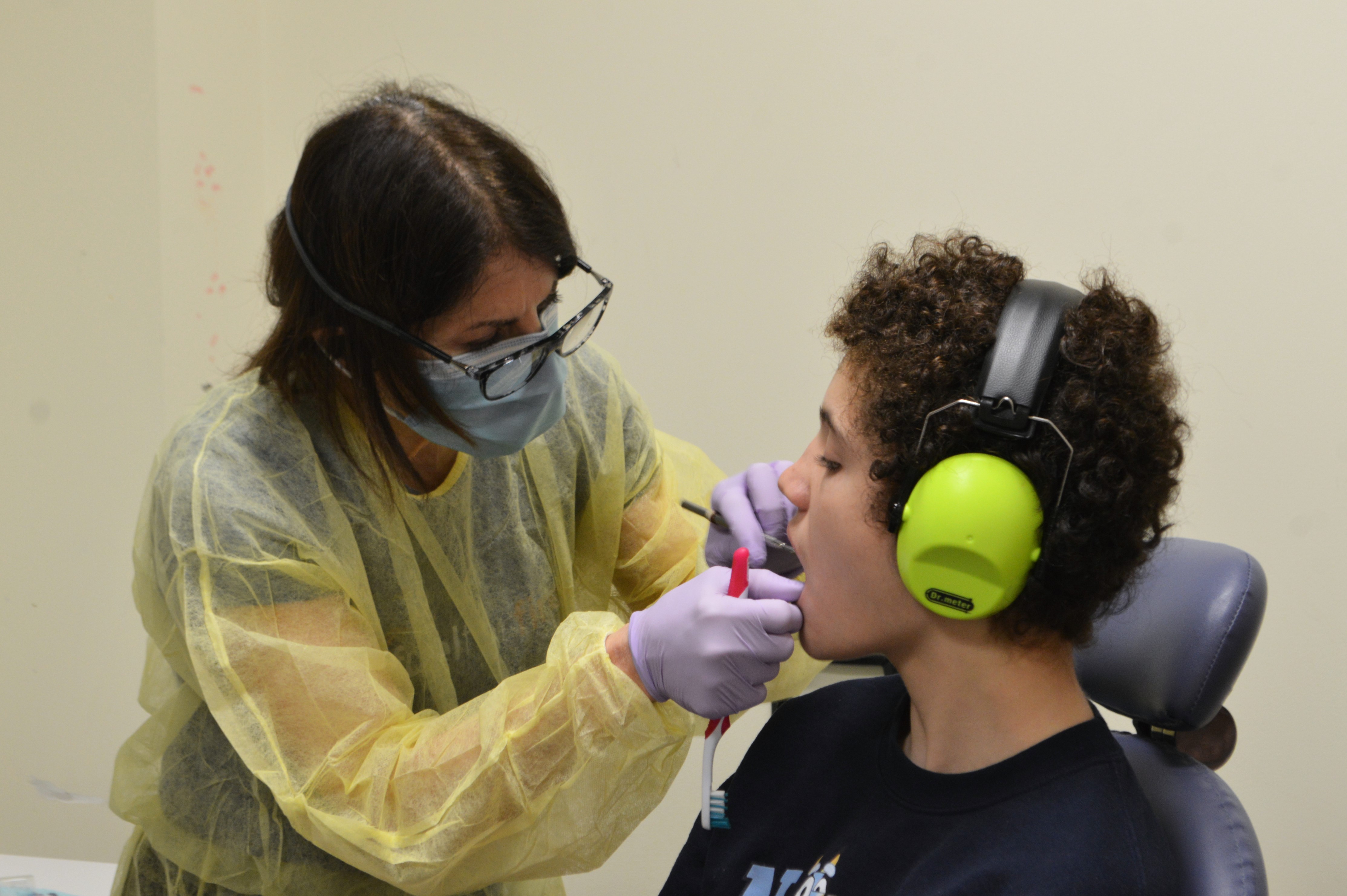 A student wearing over-the-ear headphones watches closely as a dentist flosses his teeth.