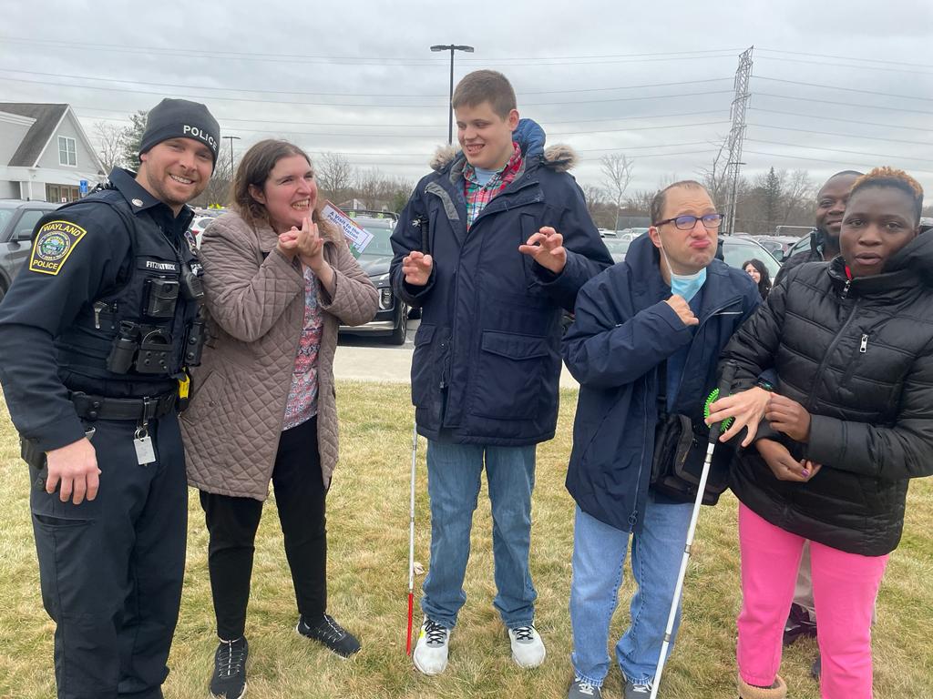 Three adult residents stand together between a police officer and a direct support staff.