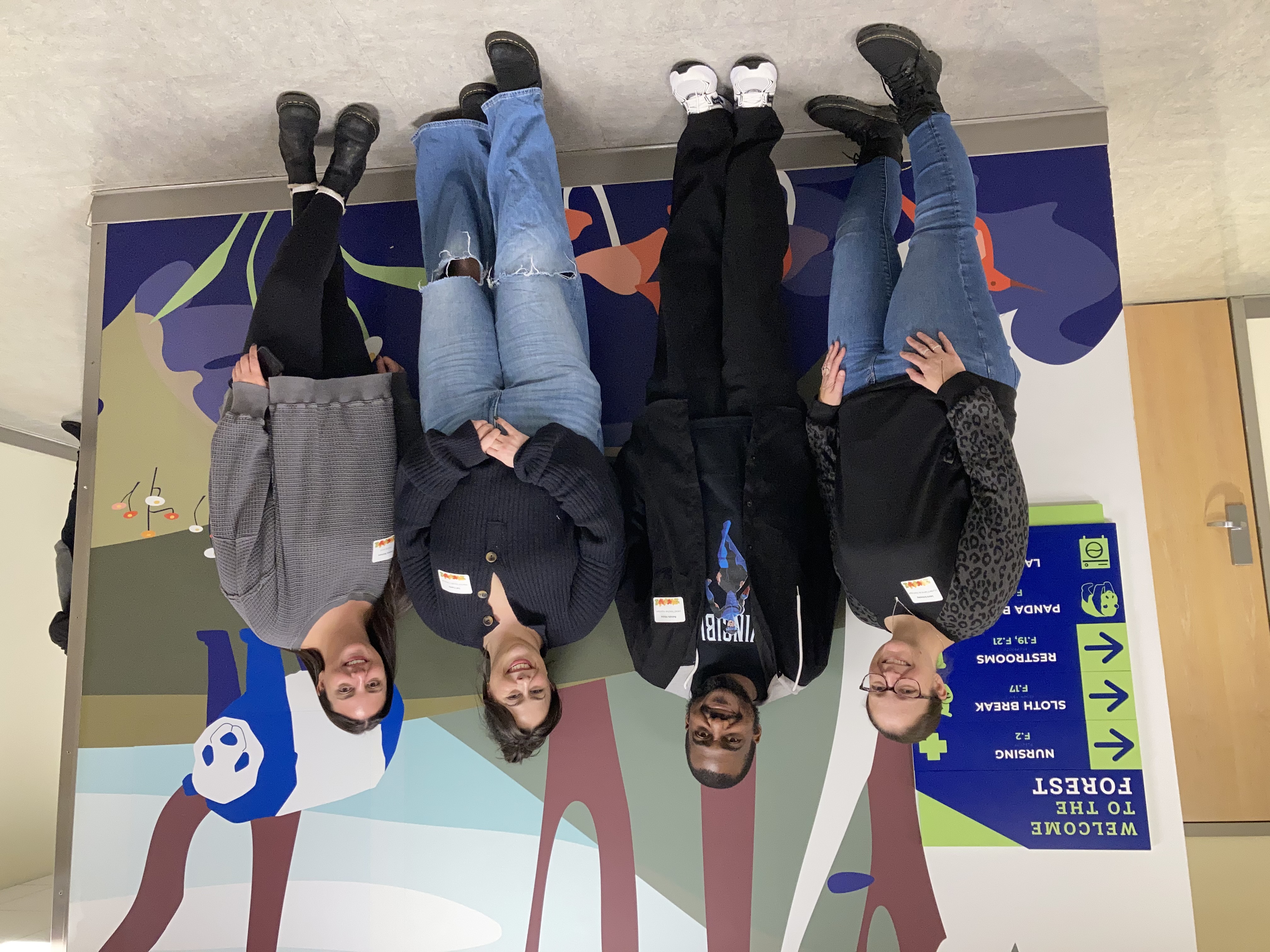 A group of 4 school staff stand together in front of a wall mural at The Guild School depicting a panda bear in the forest.