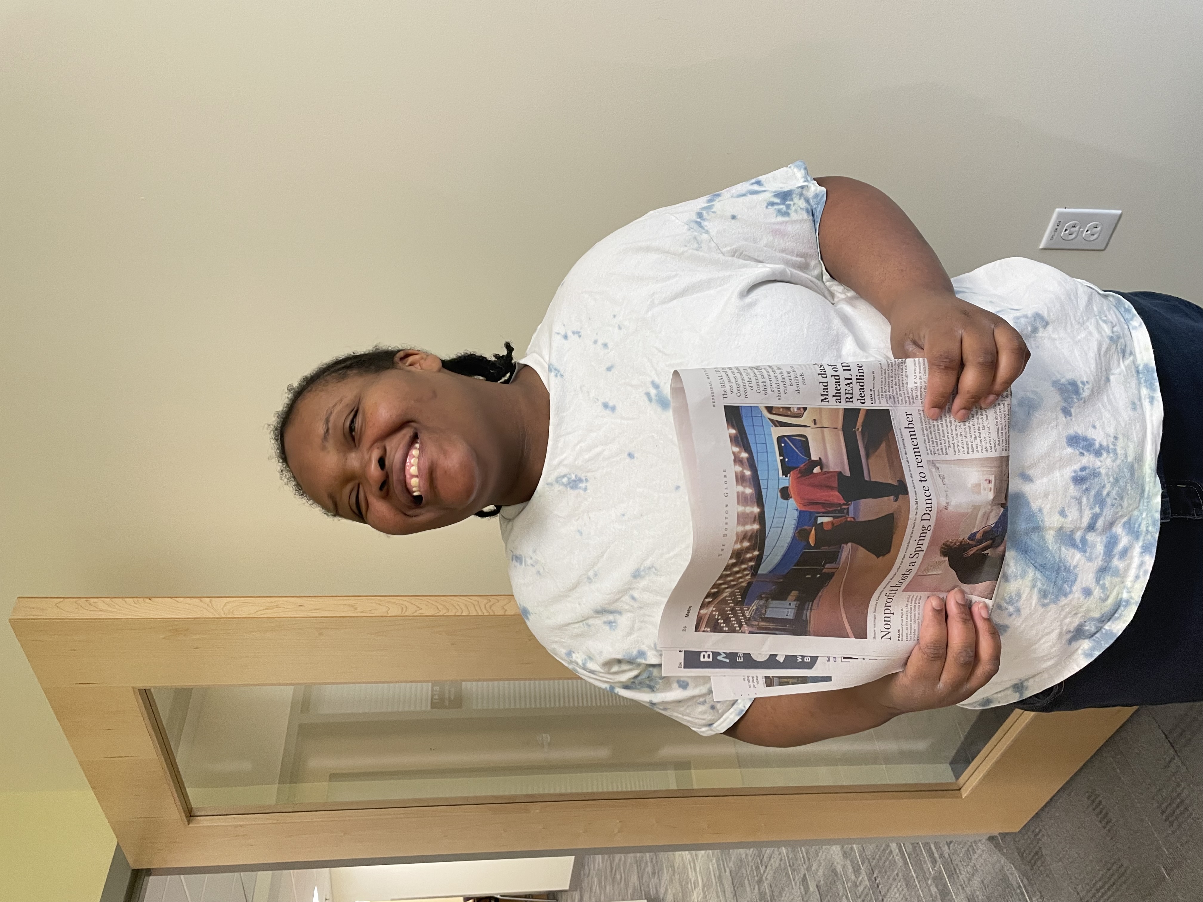An adult resident smiles widely while holding a copy of The Boston Globe newspaper.