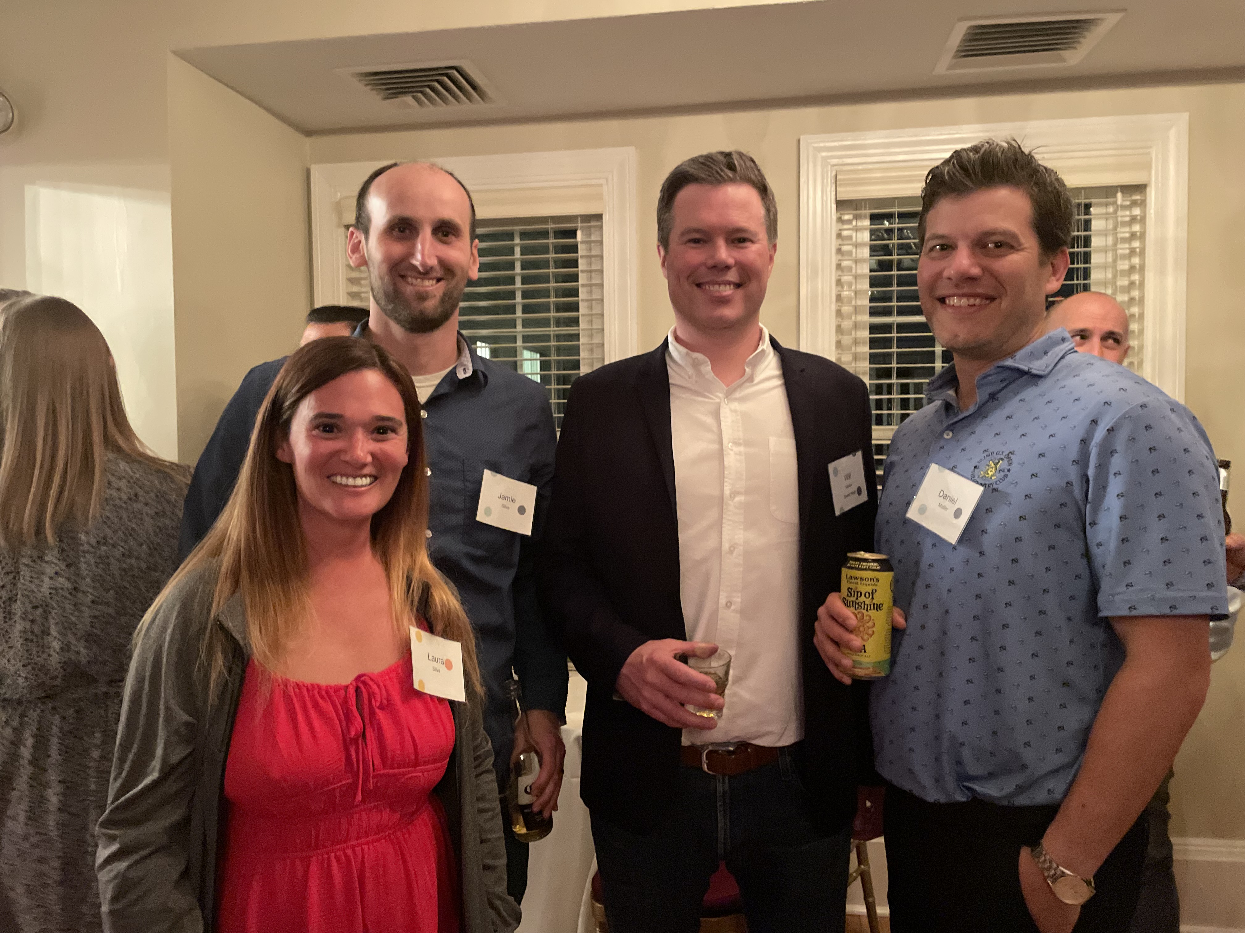A group of four people stand together in a busy room, all smiling at the camera.