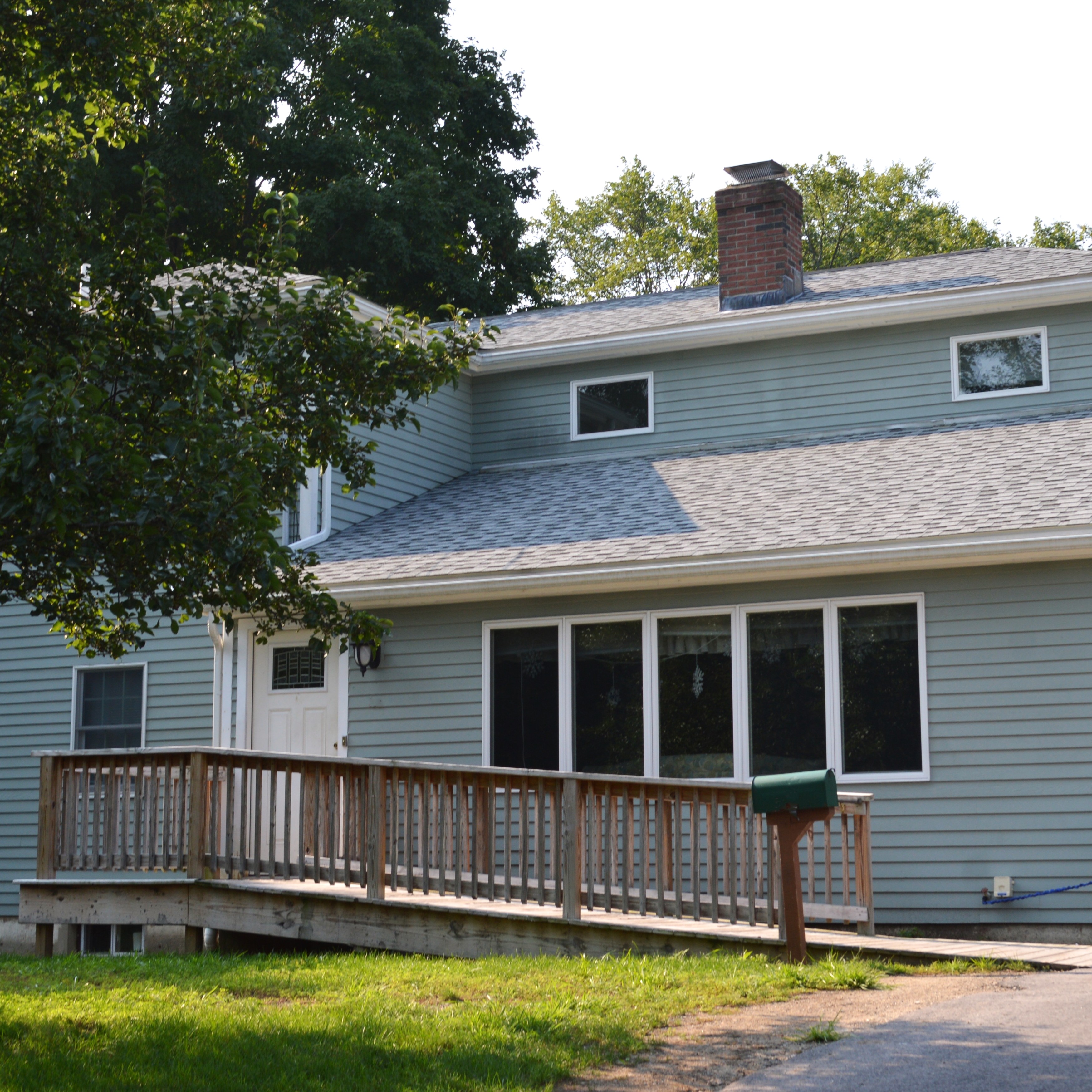 A light green house seen from the driveway with a wooden ramp leading up to the front door.