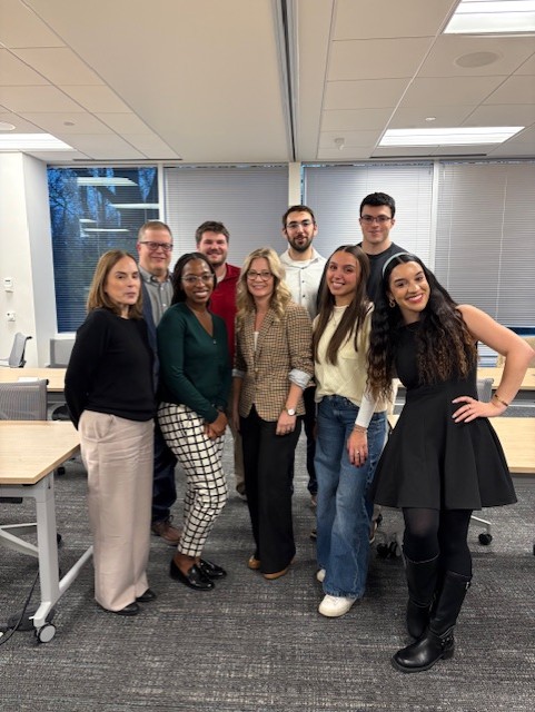 Leadership from The Guild stand together with a team of 5 Oracle-NetSuite employees in a conference room.