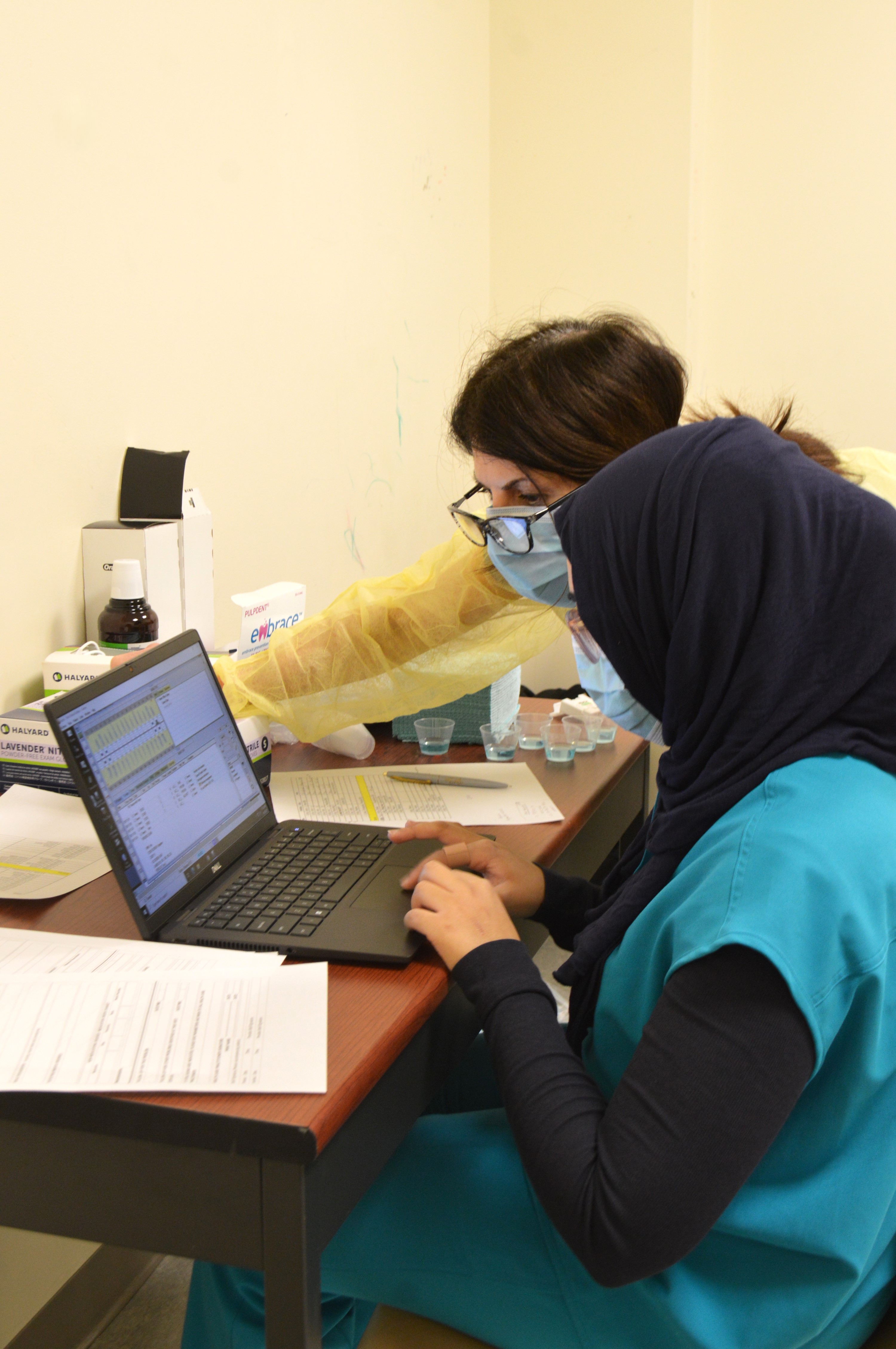 DentistsTerenzi and Islam look at a patient chart together on a laptop set up in a room for the clinic at The Guild School.