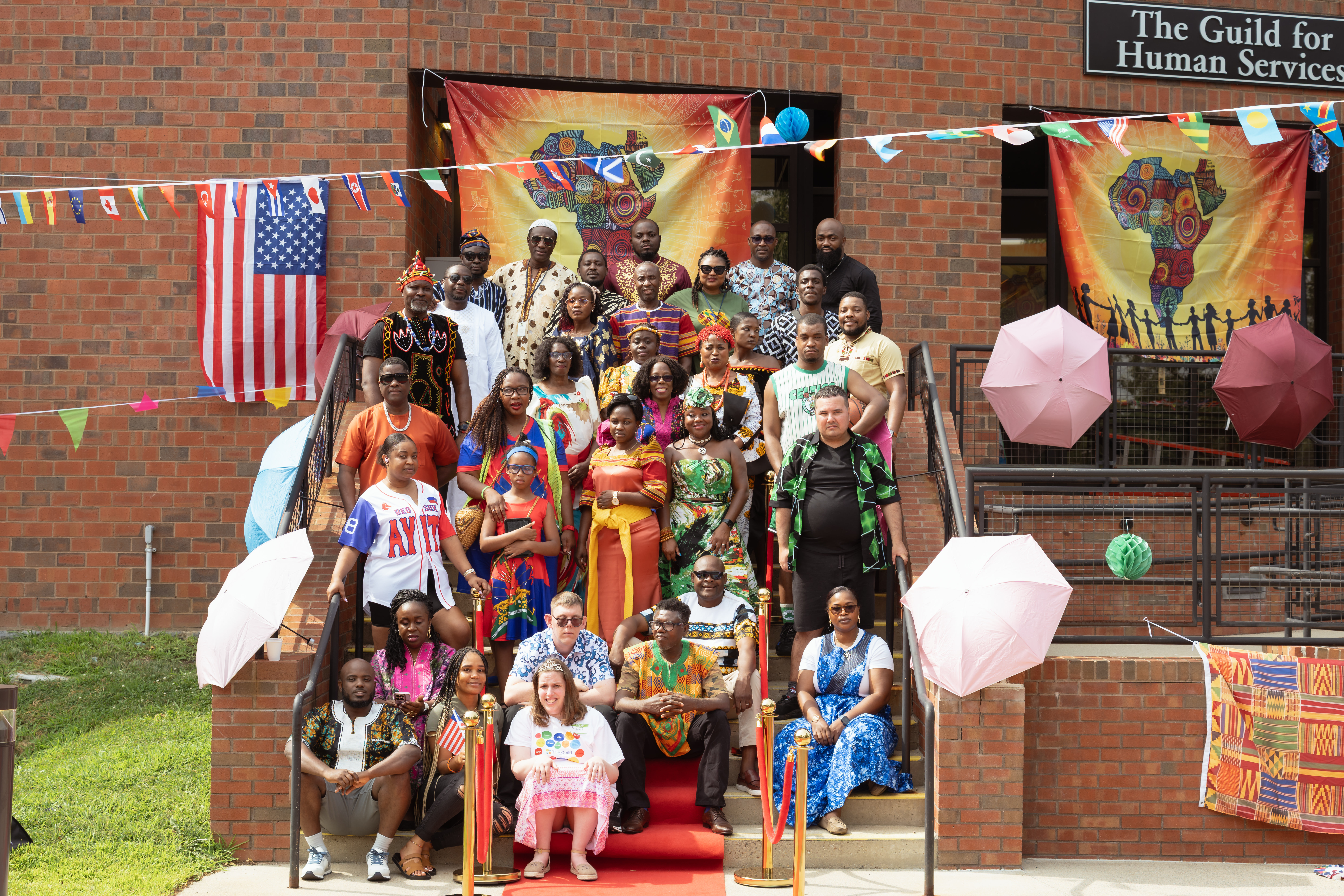 A large group of staff and a few adult residents pose together on a staircase in colorful clothing of different traditions.