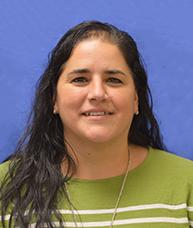 Fabiana Fickett wears a green shirt with white strips and smiles directly into the camera in front of a blue background.