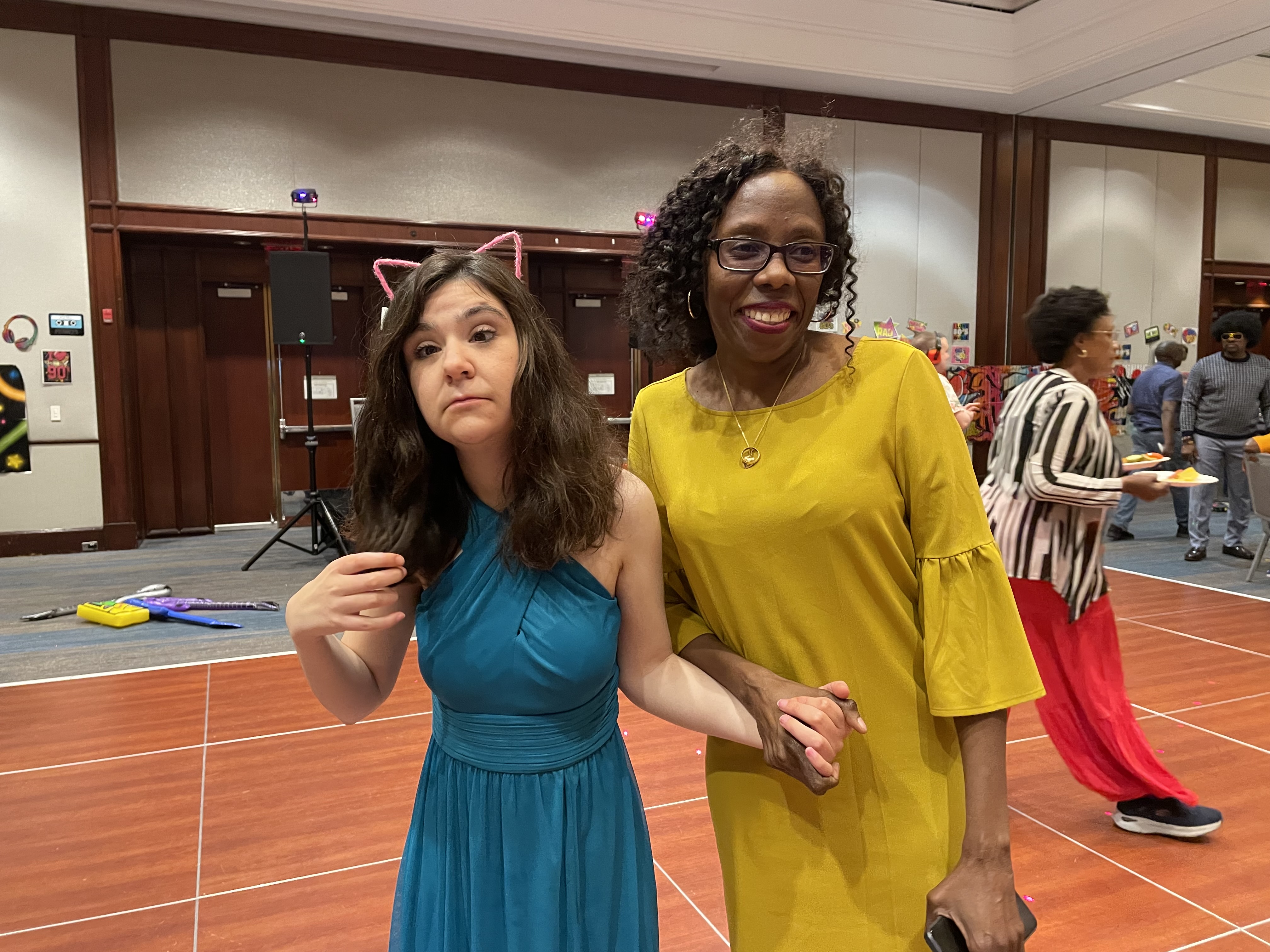 Two women, one adult resident and one youth residential staff, stand together in bright dresses on the dance floor.