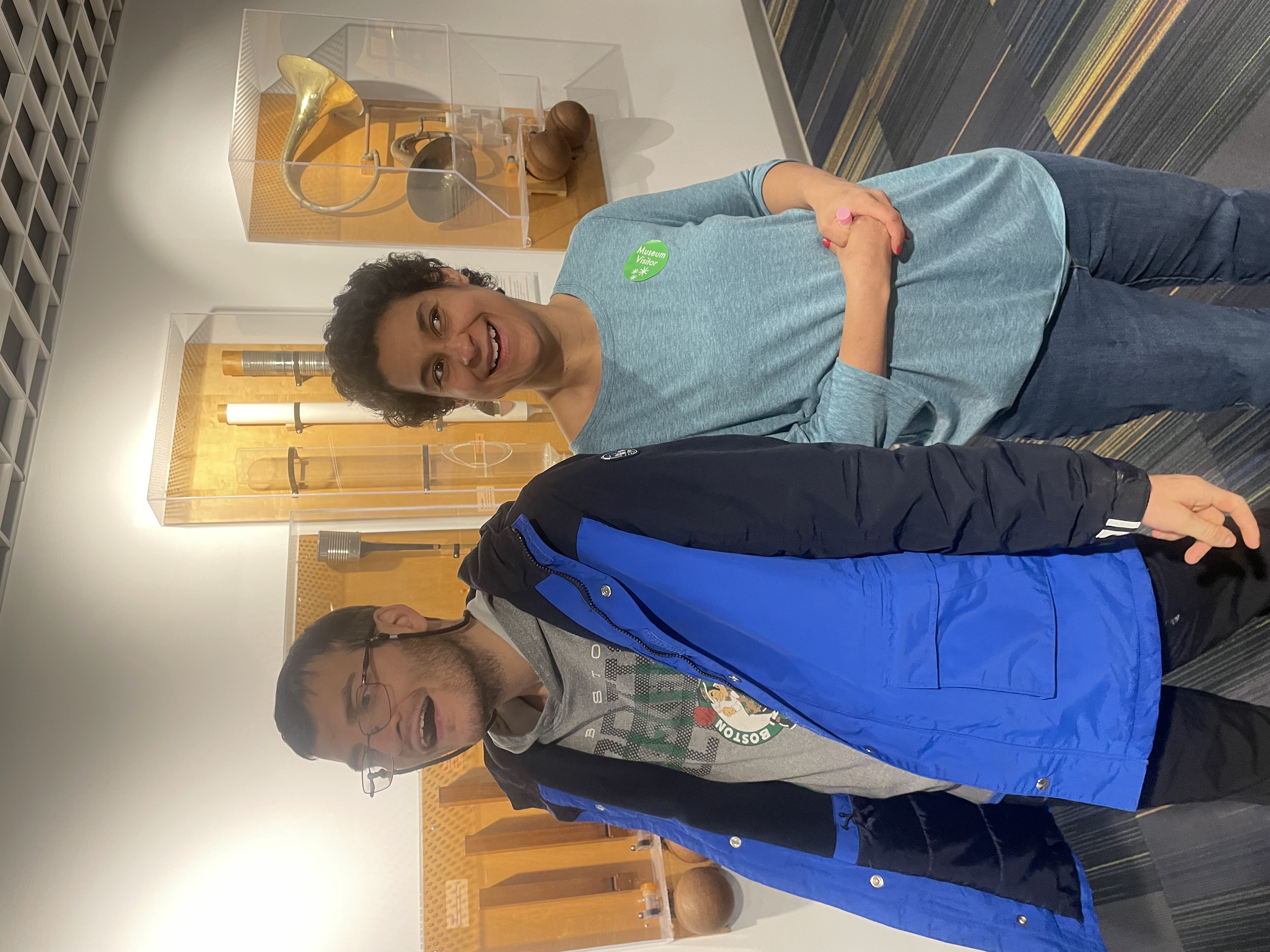 Two adult residents stand in front of interactive displays featuring objects of different sizes mounted on wooden peg boards and encased in plexiglass at the Discovery Museum.