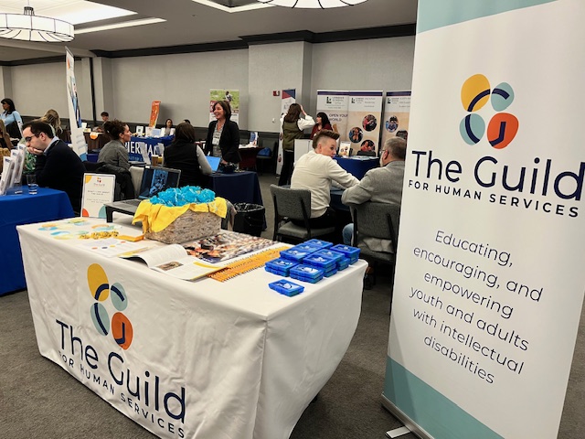 A table with a Guild tablecloth is filled with swag items in the conference exhibit hall.