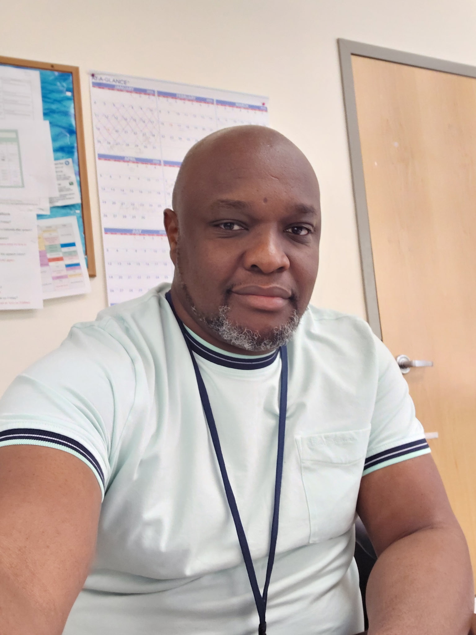 Norman Rutinwa looks casually into the camera while seated and wearing a white shirt with black accents.