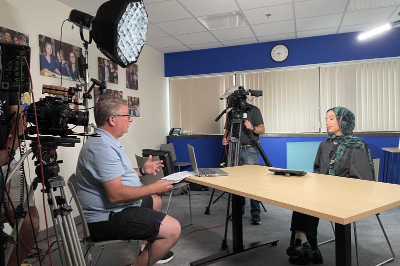 Camera equipment is set up in a small room to record an interview with a Guild staff member.