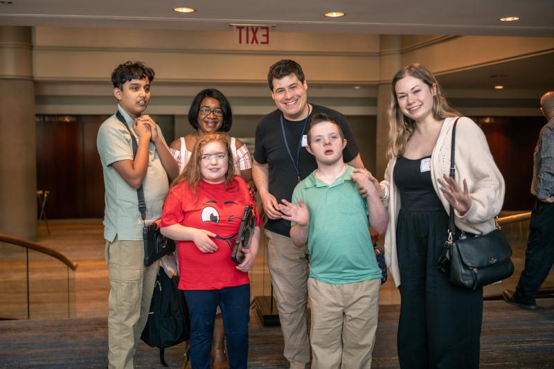 Three students stand together with classroom staff at an event in a hotel lobby.