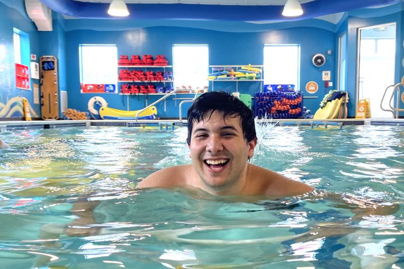 A student smiles while swimming towards the camera in a pool.