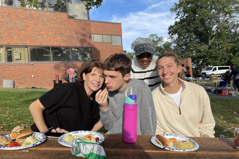 A student sits at a picnic table with two family members on either side and a residential staff standing behind them.