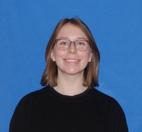 Bridget smiles into the camera in front of a plain blue wall.