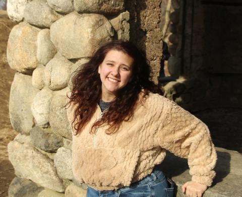 Cassie leans against a stone wall and smiles into the camera.