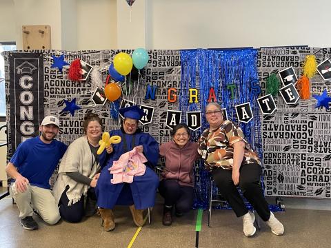 A group of staff sit together with a mom and student at her graduation ceremony from The Guild School.