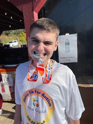 A Guild School student proudly chomps on his Flutie 5K medal after finishing the event.
