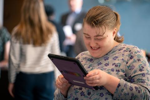 An individual smiles as she looks at her device. The screen is not visible to the camera.