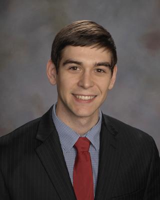 Michael Tarr sits smiling in front of a gray background, wearing a suit jacket and a red tie.