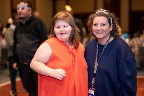 An adult resident and staff member post together at an event in a hotel ballroom.