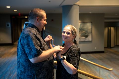 An adult resident and his mom face each other and clasp their hands together while smiling.