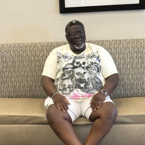 Simi Omotoye sits on a sage green bench wearing a white t-shirt and shorts.