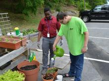 Student watering garden as staff member watches