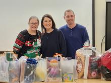 One Guild staff member stands with Michelle and Donnie Peters in front of bags of donated holiday gifts.