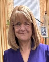 Peg Doherty is smiling and wearing a navy blue top and glasses.